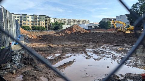 A huge muddy pit with a backhoe where apartments are being built. 