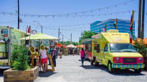 A photo of a food truck park with pink and green vehicles. 