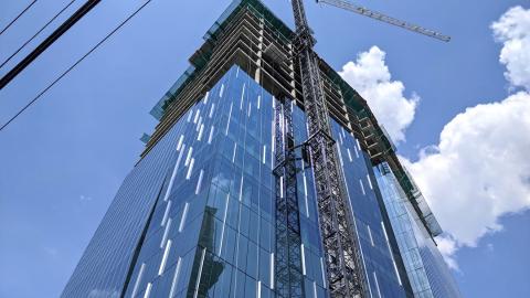 A glassy blue office tower with a crane on top being built in Midtown Atlanta. 