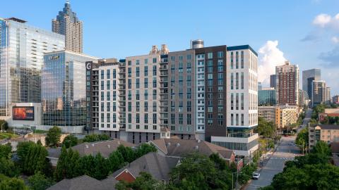 A photo of a large apartment building near downtown Atlanta skyrises under blue skies. 