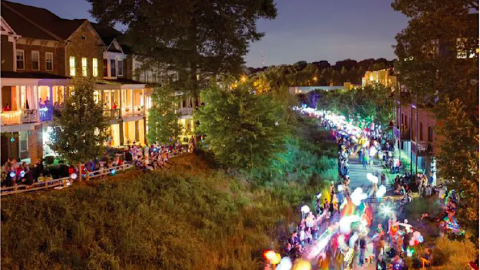 An image of a large parade with people with lanterns beneath a night sky. 