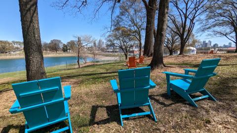 A photo of a park beside a lake with blue and orange chairs and Atlanta's skyline beyond. 