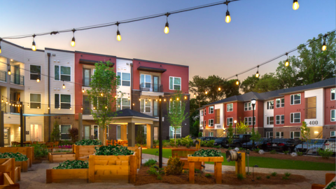 A photo of a long low apartment complex under bluish skies with surface parking lots at the corners.