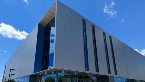 A new sleek modern building with gray panels and large glass windows under a blue sky.
