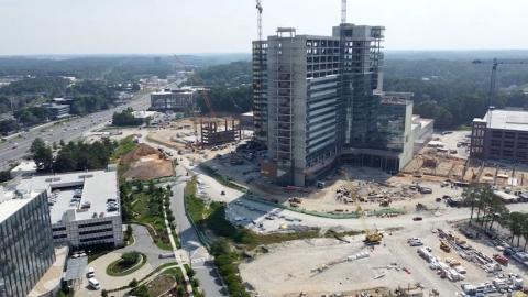 An image of a huge hospital project under construction against rolling hills and trees in summertime Atlanta. 