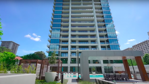 A photo of a large glassy white condo tower over trees with a pool and yard behind it in Buckhead Atlanta. 
