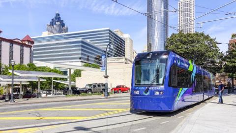 A photo showing a purple blue train under blue skies in downtown Atlanta. 