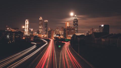 A photo of a skyline under the moon of Atlanta at night with red car lights on a highway.