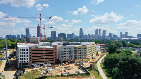 An aerial view of a large apartment and office development on the Atlanta Beltline with the city skyline in the background.
