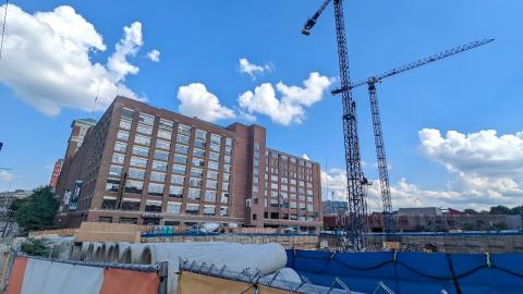 A photo of a huge brick building with two massive cranes reaching into the sky over an excavation pit.