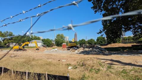 A construction site surrounded by barbed wire in Atlanta with yellow heavy machinery on site near a park.