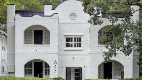 A photo of a white two-story apartment building in the Spanish Mission-style in Atlanta near many trees.