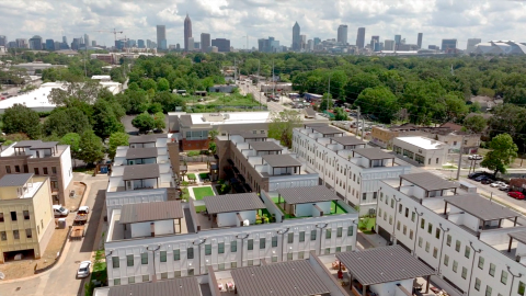 An aerial photo of a row of white and brick townhomes with brown roofs under construction in Atlanta with the skyline in the distance.