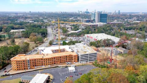 A drone image of a large construction site with a wooden apartment building and concrete parking structure behind it.
