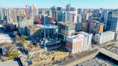 A photo of a skyline with many buildings and many large red cranes under a blue sky in Atlanta near busy highways. 