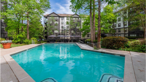 A photo of a gray and white apartment complex under blue skies with many bushes. 