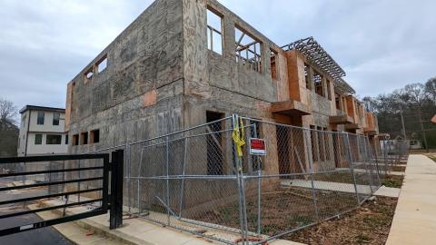 A photo under gray skies of a townhome project with gray plywood and new homes behind them.