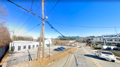A site under blue skies scheduled for development in Atlanta, next to a two-lane road with cars.