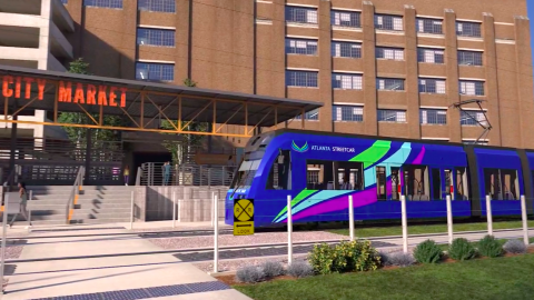 A rendering of a bluish purple Atlanta streetcar near a huge brick building under blue skies.