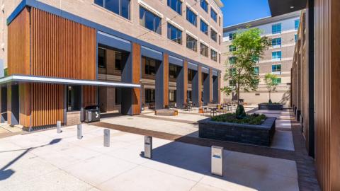 A renovated mid-rise office building under blue skies with new wood slats near bench seating and a street.