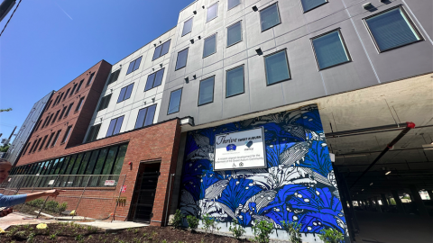 An image of a brick mid-rise building with a large parking deck and a blue mural on the front.