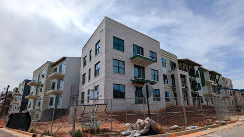An image of a large development with brick and glass and a mix of townhomes and apartments under blue skies next to an airport.