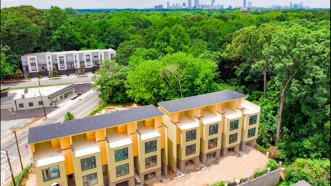 An image showing a row of new modern townhomes with large rooftops near many trees and tall buildings.
