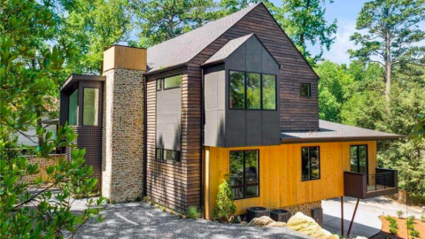 A photo of a modern new home with rustic elements like stone and wood on a steep lot under blue skies, with a spacious new white interior.