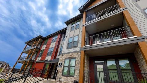 a photo of an apartment complex built with stone and wood under blue cloudy skies with a large pool in the middle. 