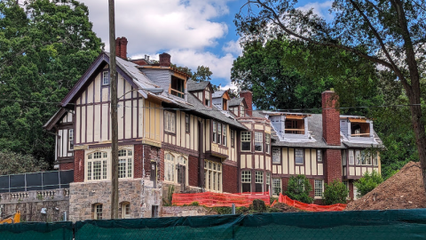 An image of a large historic property with a Tudor mansion under blue skies with many trees around it, and much construction.