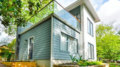 An image of a small two story house with glass-rail balcony and white interiors.