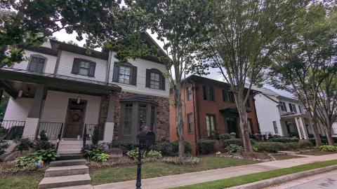 A photo of a row of house with many trees under gray skies, with sidewalks in front. 