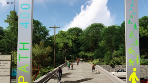 An image of a walking and bike trail with a high metal arch at the entrance. 