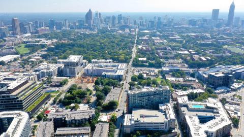 An aerial photo of a large city under blue skies with many trees and tall buildings.