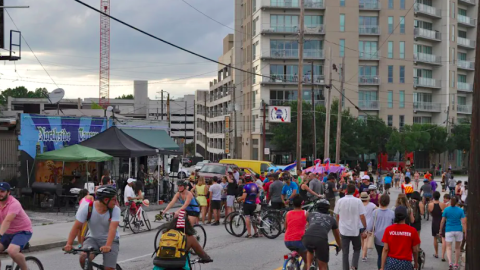 A photo of many people on bikes and walking in a street in Atlanta near tall buildings.