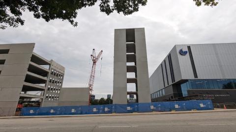 A photo of a large standalone parking garage under construction next to a modern gray building under gray skies. 
