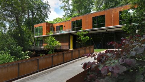 A modern house with airy white interiors built of corten steel on the outside with a bridge in front. 