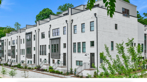 A photo of a white-brick new townhomes and standalone home development under blue skies in Atlanta.