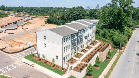 A photo of a large new row of townhomes near mounds of dirt and tall trees under a blue sky in Atlanta.
