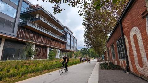 A photo of a long black building with many patios under gray dark skies beside many trees and a wide concrete trail.