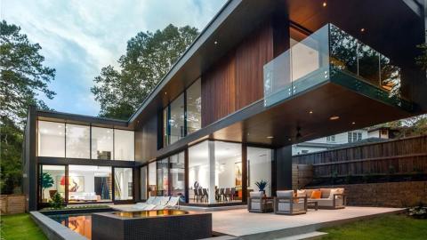 A black and wood clad two-story modern house under blue gray skies with a pool and hot tub shown in Atlanta, with white interiors and black kitchen.