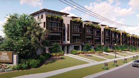 An image of a large brown and beige townhome development under blue skies near a wide road.