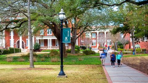 A photo of people walking through a college campus near many trees. 