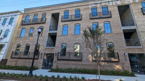 A photo of a large new brick building with rows of townhomes beside it under blue skies in Atlanta.