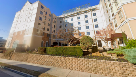 An image of a standard beige and brown hotel under blue skies in Buckhead Atlanta near a wide street.