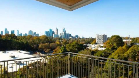 An image showing a large white new condo unit with a large patio and views over treetops to Midtown Atlanta. 