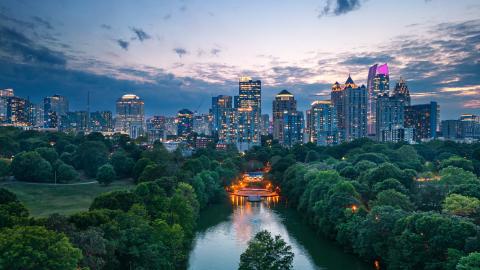 An image showing a green park near a lake with a large lovely skyline in the distance.