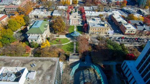 An aerial photo of a downtown with many buildings positioned around a square with many trees.