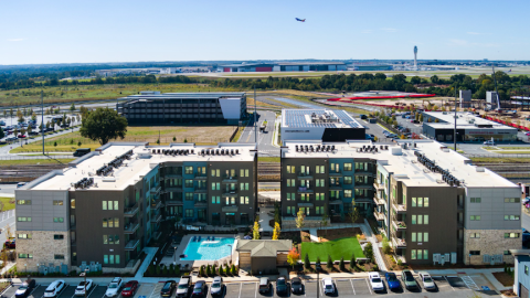 An overview photo of a large apartment development with many new buildings around a parking lot with a dog park and pool in the middle.