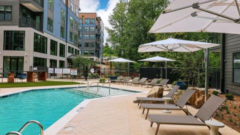 An image showing a gray and wood clad apartment complex with a large pool and modern-style interiors with a rooftop deck in Atlanta.